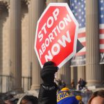 person holding red Stop Abortion Now signage